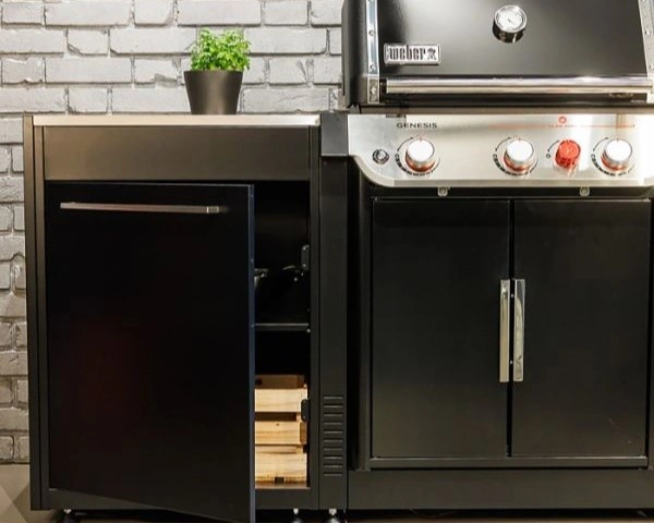Parte din bucatarie exterior BBQ Kitchen cu gratar genesis si modul cu dulap cu usa deschisa si lemne in dulap.